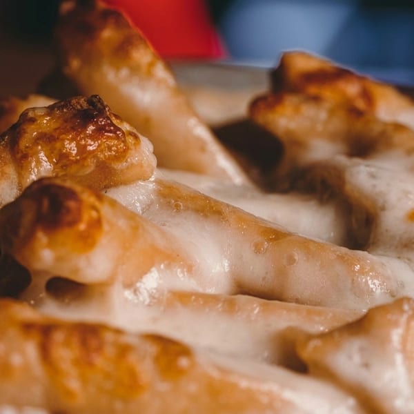 Close-up of golden-brown breadsticks covered in melted white cheese, glistening under warm light.