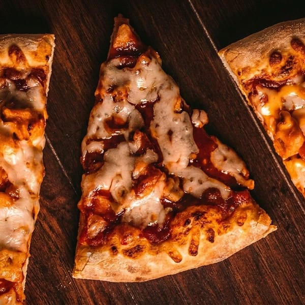 Three slices of pizza with melted cheese and various toppings on a dark wooden surface.